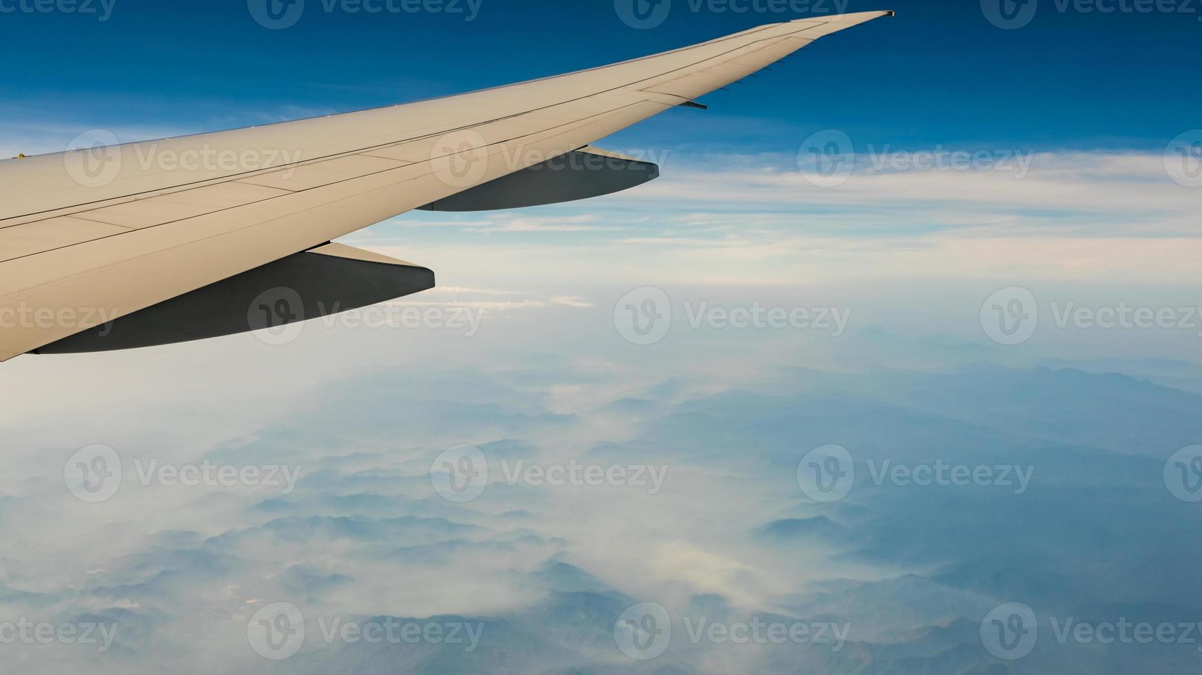 ala de avión sobre la cubierta montañosa con niebla y neblina. avión volando en el cielo azul. vista panorámica desde la ventana del avión. vuelo de aerolínea comercial. ala de avión mecánica de vuelo. Vuelo internacional. foto