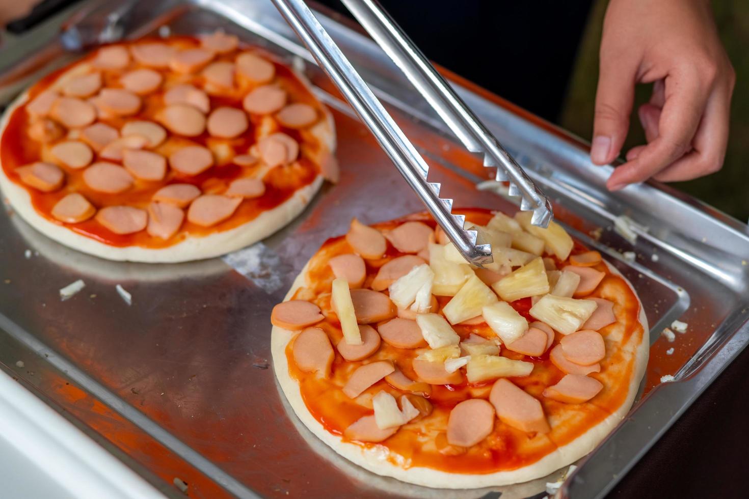 Man make pizza for donate at charity event with pizza crust and pineapple. Female chef preparing pizza with hands putting the ingredients for the pizza in tray on the wooden table . Food preparation. photo