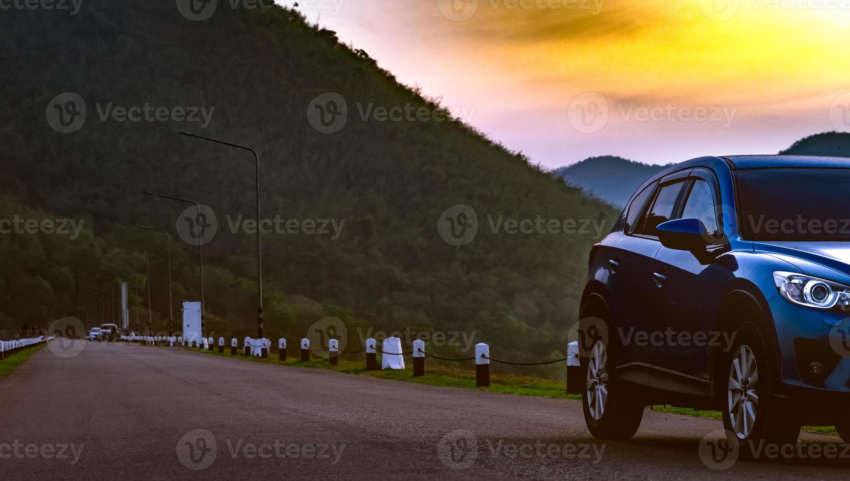 Blue SUV car parked on asphalt road in front of the mountain. Car parked at the park in early morning with sunrise sky. Road trip travel. Car parking space. Automotive industry. Nature tourism. photo