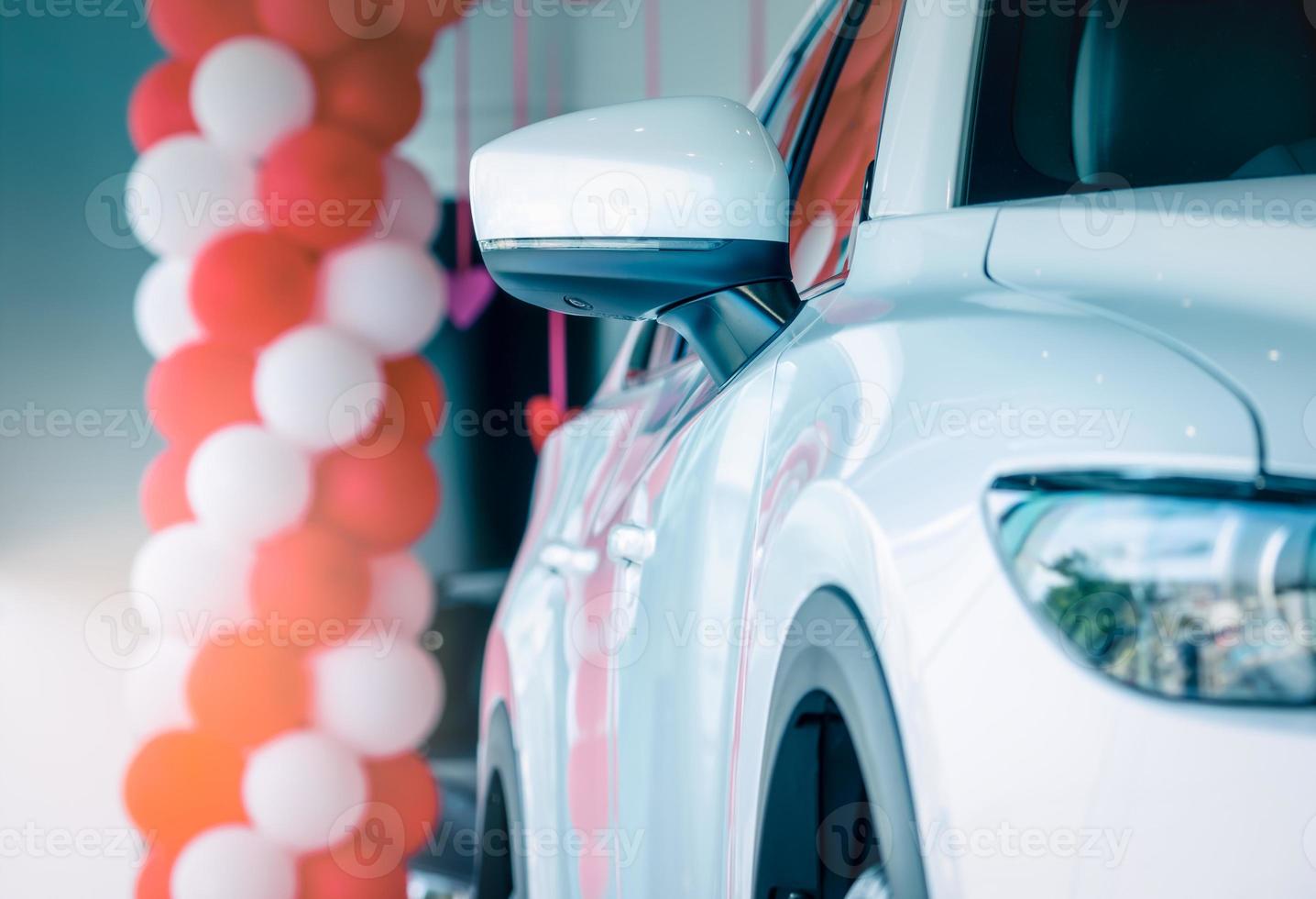 Side mirror white car parked in modern showroom. New and luxury compact car. Car dealership concept. Automotive industry. Automobile leasing business. Front view of white shiny car parked in showroom. photo