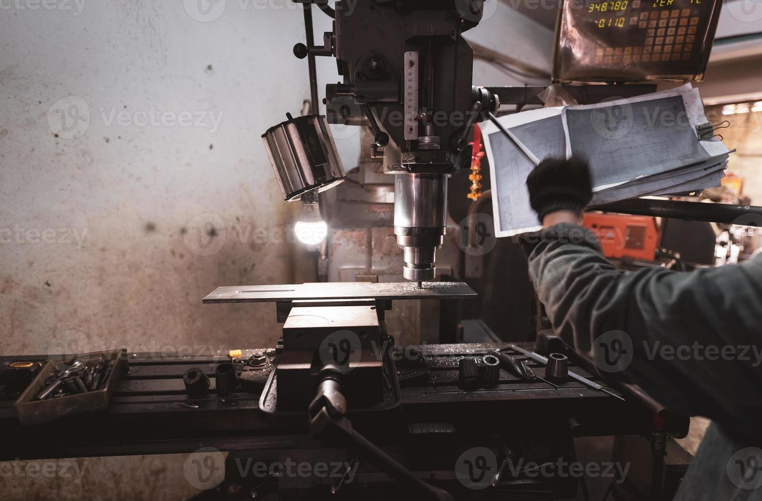 Milling machine working near worker with gloves. Tool for cut metal workpiece. Vertical milling machine with cemented carbide milling cutter. Steel manufacturing industry. Milling process. Metalwork. photo