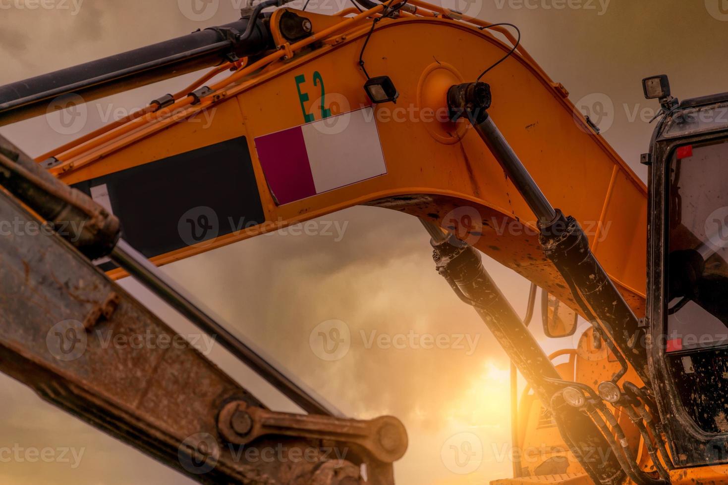 Closeup hydraulic piston arm of dirty backhoe at construction site. Yellow excavator parked at construction site against sunset sky. Digger machine. Hydraulic machinery. Excavator for rent business. photo