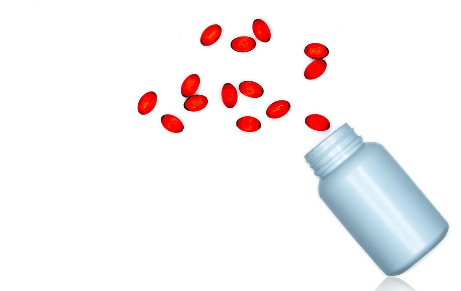 Pour red soft gel capsule pills out of drug bottle isolated on white background. Red soft gelatin capsule vitamins and dietary supplements. Pharmaceutical industry. Pharmacy drug store. Healthcare. photo