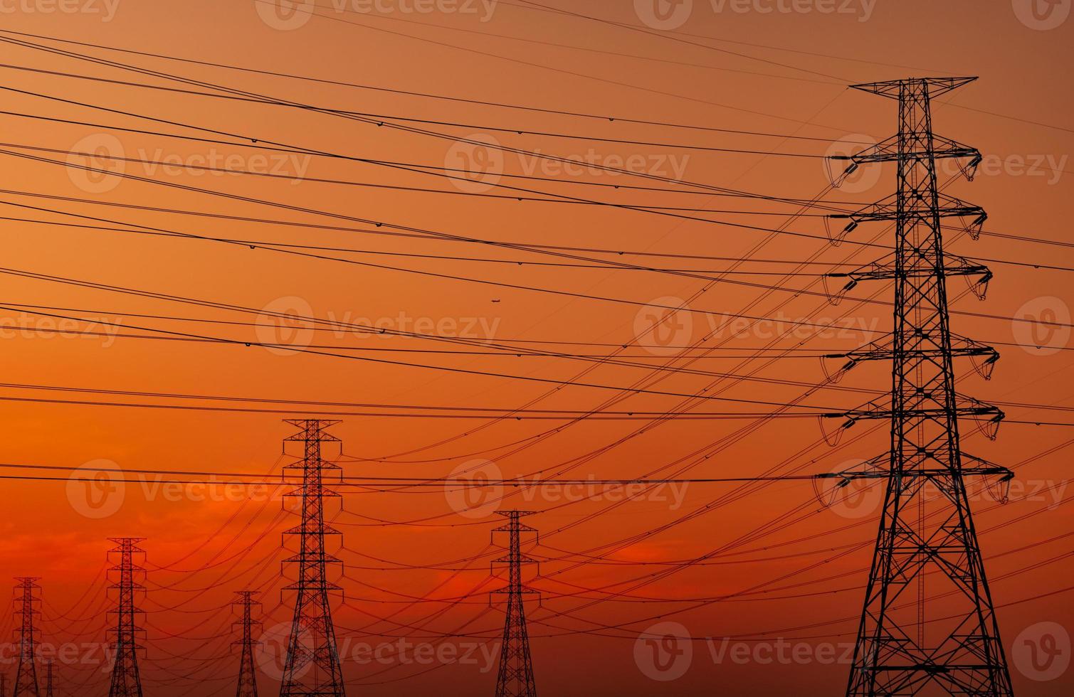 Siluetee la torre eléctrica de alto voltaje y el cable eléctrico con un cielo anaranjado. postes de electricidad al atardecer. concepto de potencia y energía. torre de red de alto voltaje con cable de alambre en la estación de distribución. foto