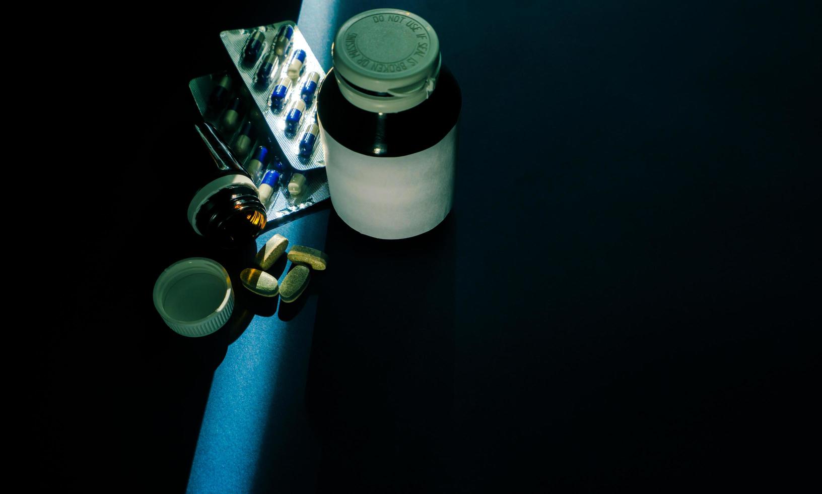 Capsules and tablets pills with amber bottle on dark blue background with copy space. Medicine and supplements interactions concept. Drug use with reasonable and global healthcare concept. photo