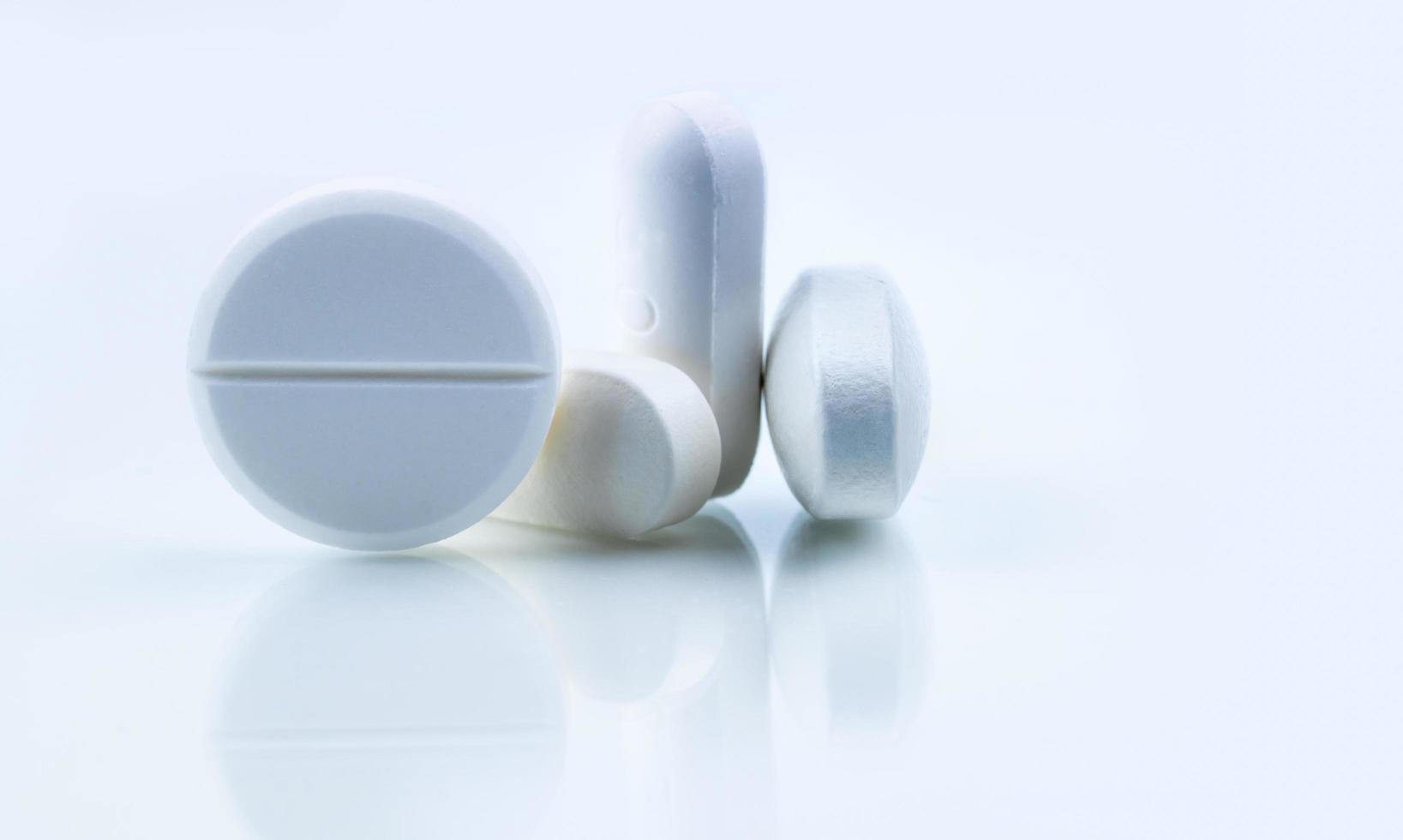 Round and oval white tablets pills on whit background. Selective focus on white tablets pills. Pharmaceutical industry. Drug production. Pharmacy drugstore products. Pharmaceutical manufacturing. photo