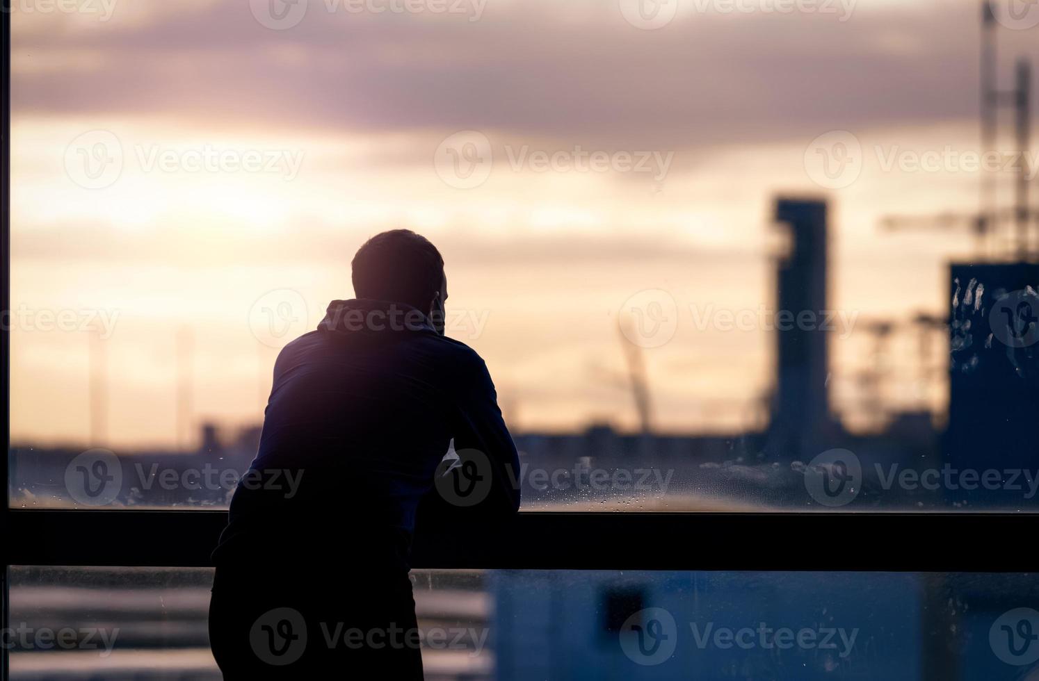 Back view of a man standing and looking through glass window of the airport building to outside. Thinking man. Rear view of a man wear protective face mask waiting for the flight. Travel alone. photo