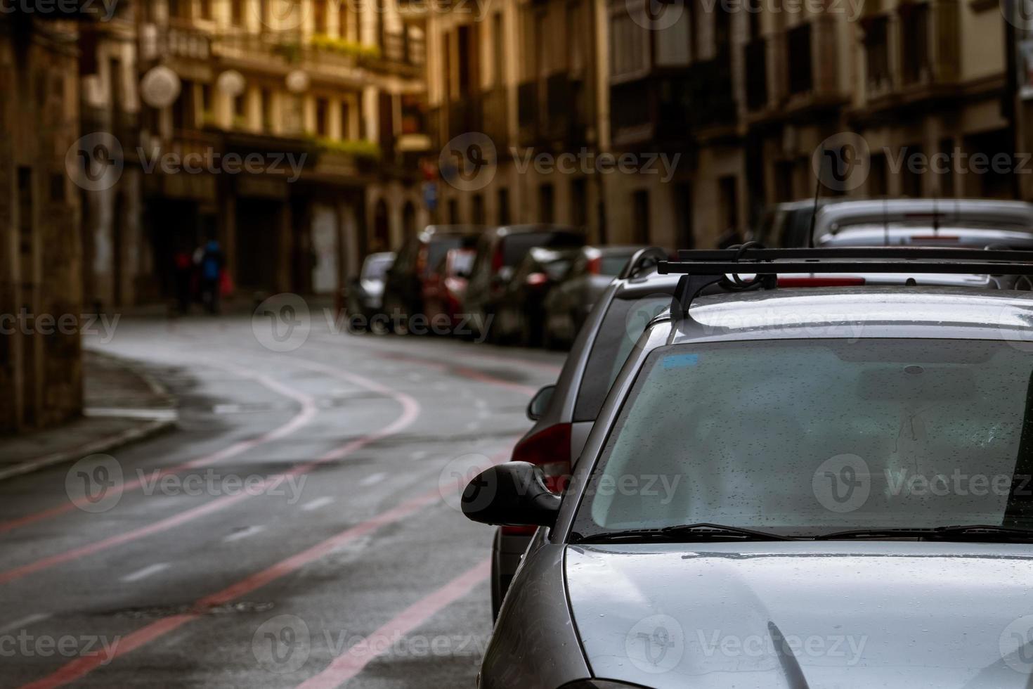 Row of cars parked along the street and old buildings in Europe city. Many cars parked on road in old town. City street in Europe. Front view of car parked outside residential building. City traffic. photo