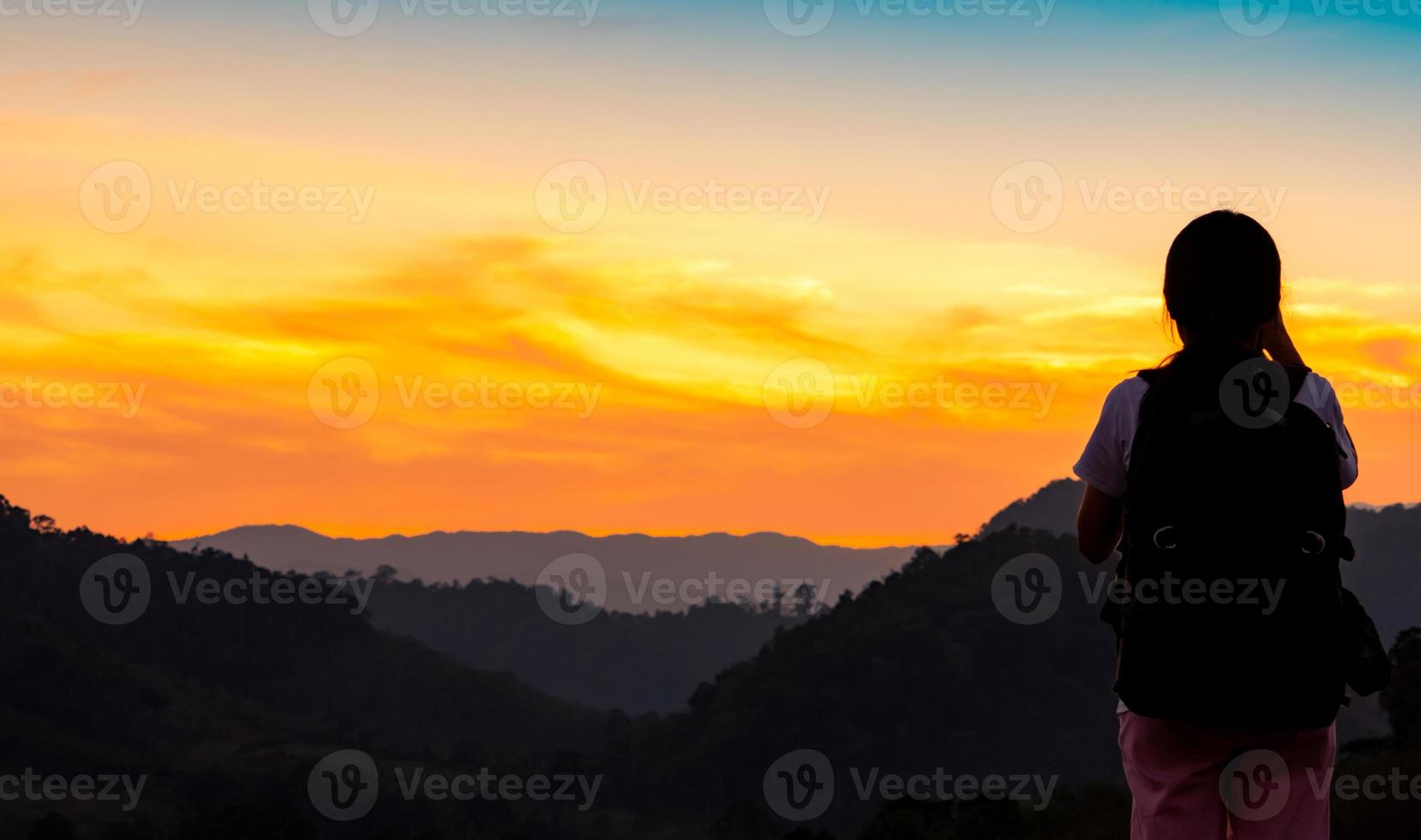 vista trasera de una joven viendo la hermosa puesta de sol sobre la capa montañosa. mochilero feliz de viajar solo. silueta de senderismo turístico a la cima de la montaña. actividad de aventura de niña activa. foto
