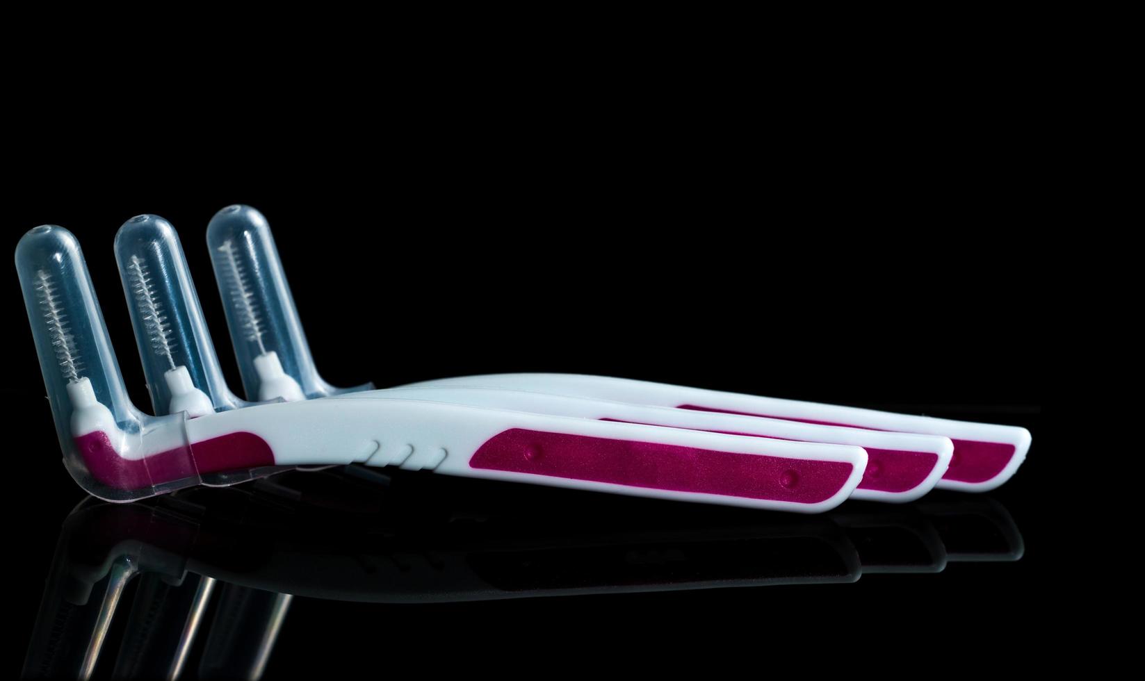 Three interdental brush with cover isolated on dark background with copy space. Dental care concept. Equipment for get rid of food stuck in teeth photo