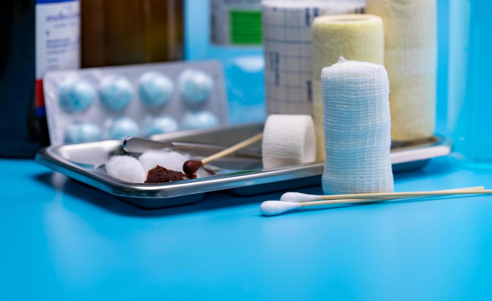 Wound care dressing set. Selective focus cotton stick and elastic conforming bandage, stainless steel plate on blur forceps, bandage, cotton ball with alcohol. Medical supply on blue background. photo