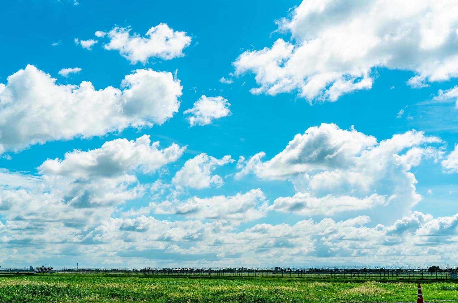 Landscape green grass field and wire fence of the airport and beautiful blue sky and white fluffy clouds. Nice weather. Nature landscape. Area around the airport. Fence for safety. photo