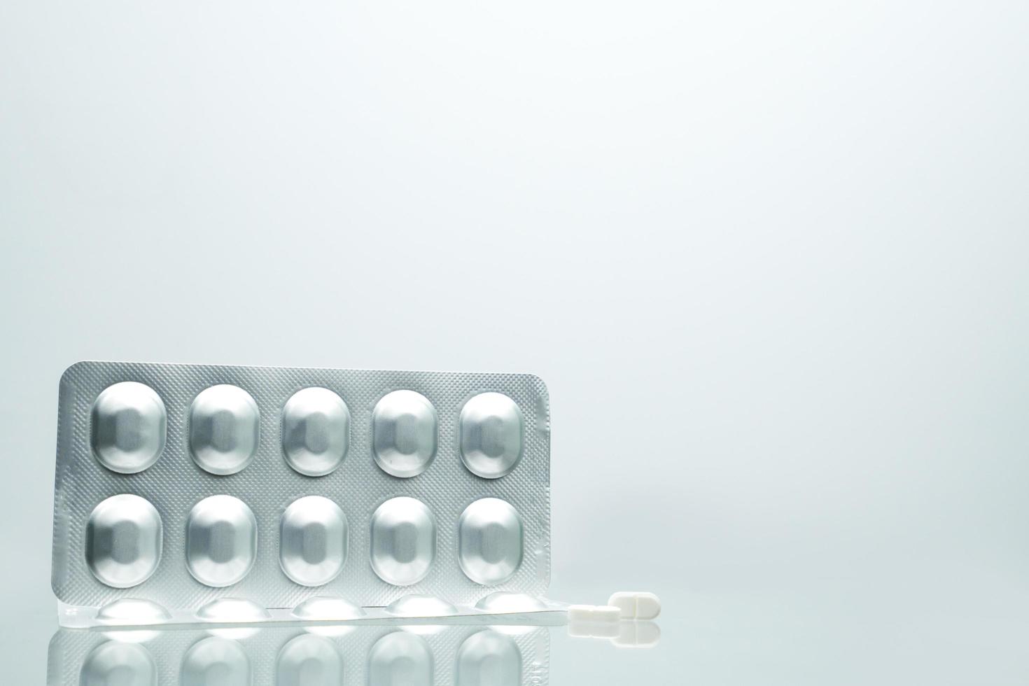 Silver aluminium foil blister pack of pills with 2 white tablet pills on white background with shadows and copy space for text. Pharmaceutical packaging and medicine storage concept photo