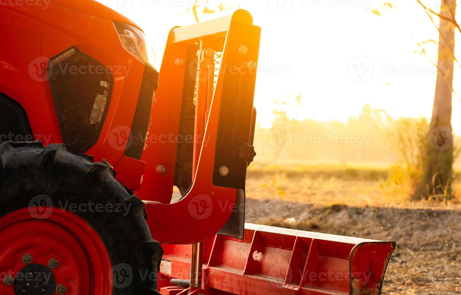 tractor naranja estacionado en una granja de arroz en la mañana de verano con luz solar. maquinaria agrícola en granja agrícola. concepto de agricultura inteligente. vehículo en finca. Maquinaria que ahorra mano de obra. equipo para plantación foto