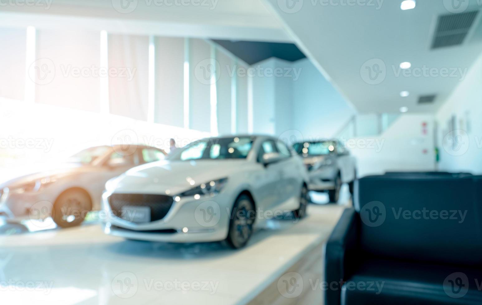 Blurred front view of white car and customer. New luxury car parked in modern showroom. Car dealership office. Electric car business concept. Automobile leasing. Showroom interior building design. photo