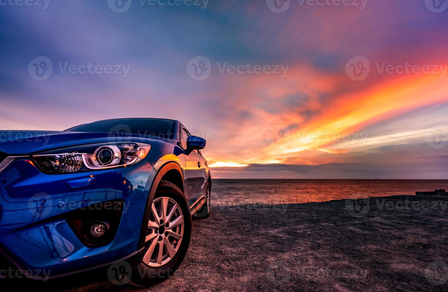 Blue compact SUV car with sport and modern design parked by beach at sunset. Hybrid and electric car technology. Car parking space. Automotive industry. Car care business background. Beautiful sky. photo