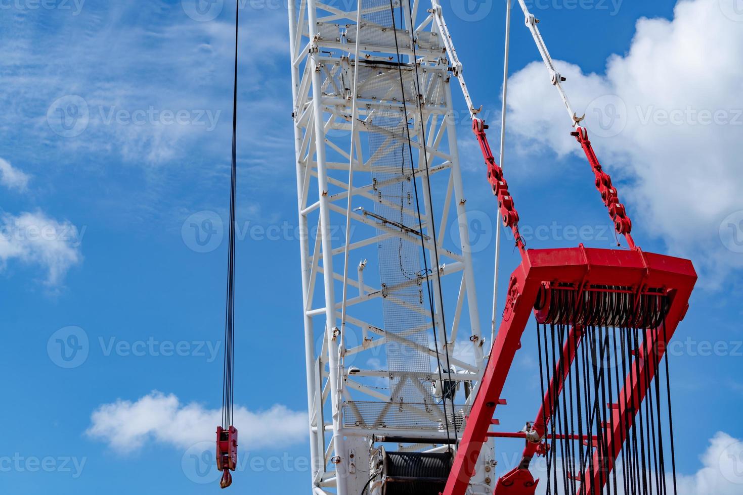 Crawler crane against blue sky and white clouds. Real estate industry. Red-white crane use reel lift up equipment in construction site. Crane for rent. Crane dealership for construction business. photo