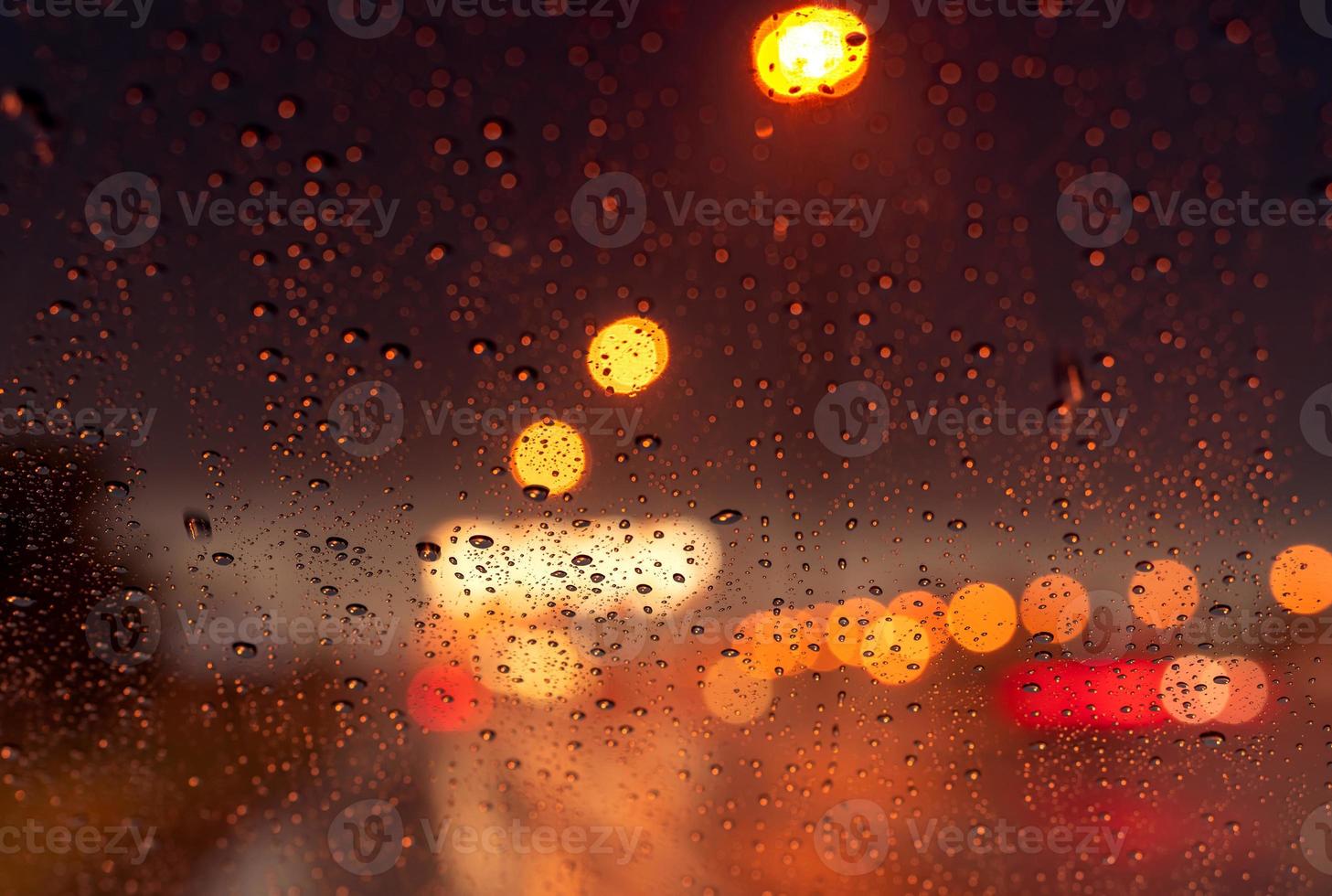 Orange night light bokeh from street light on traffic jam day. Rainy day. Transparent glass window with rain drop. Romantic weather. City life. Blur abstract background of urban light on rainy season photo