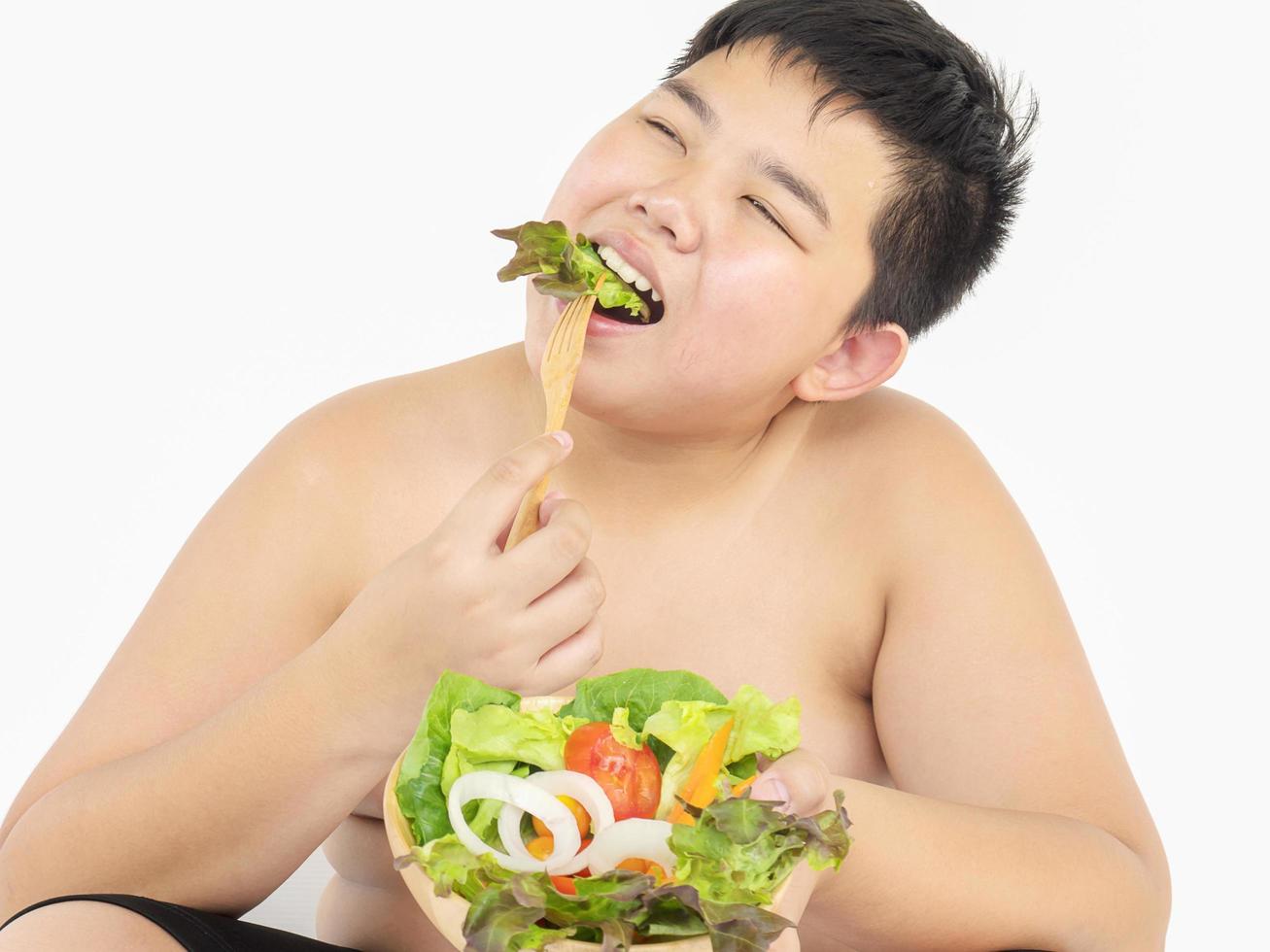 A fat boy is happily eating vegetable salad photo