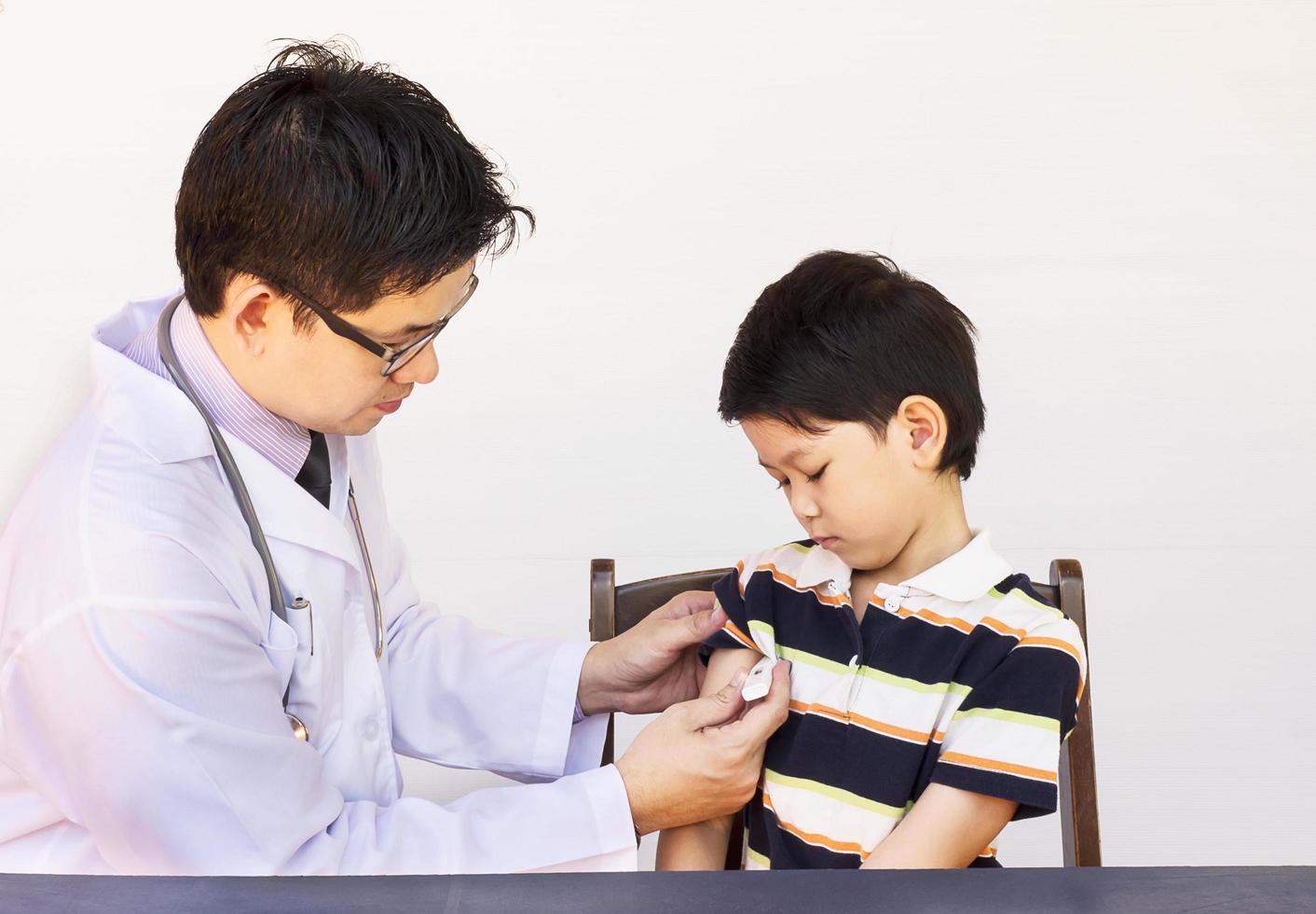 Sick Asian boy being examined by male doctor over white background photo