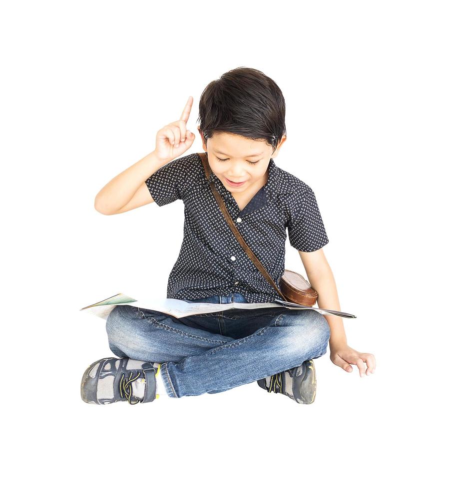 7 years old Asian traveler boy is happily sitting and looking at a map while pointing up his index finger isolated over white photo