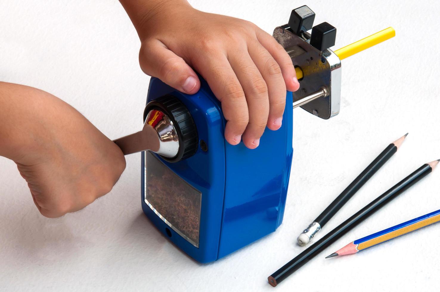 A boy is sharpening his pencil using mechanical sharpener over white background photo