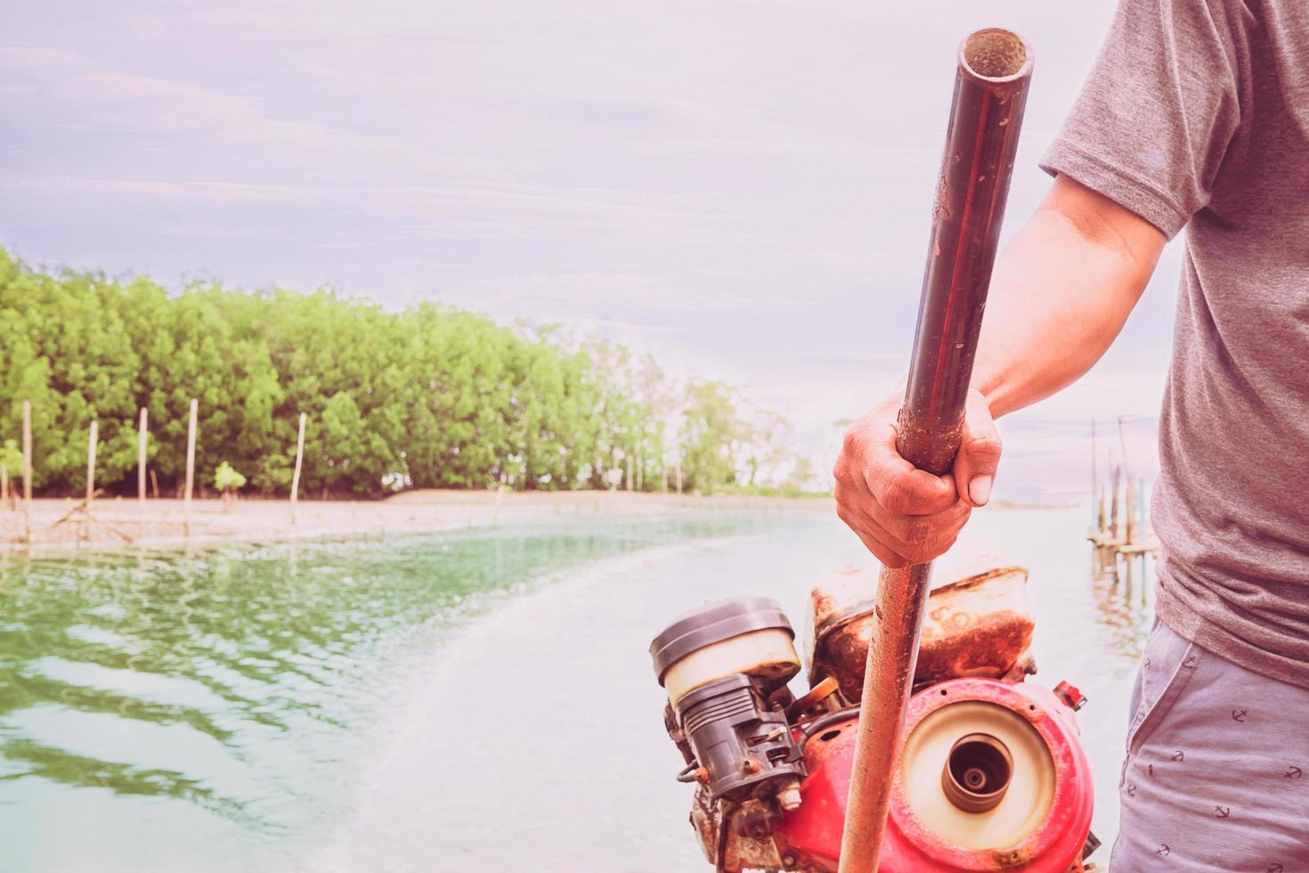 Vintage style photo of a fisherman is controlling rudder engine on a boat in the river mount near to the sea with mangrove forest and blue sky background