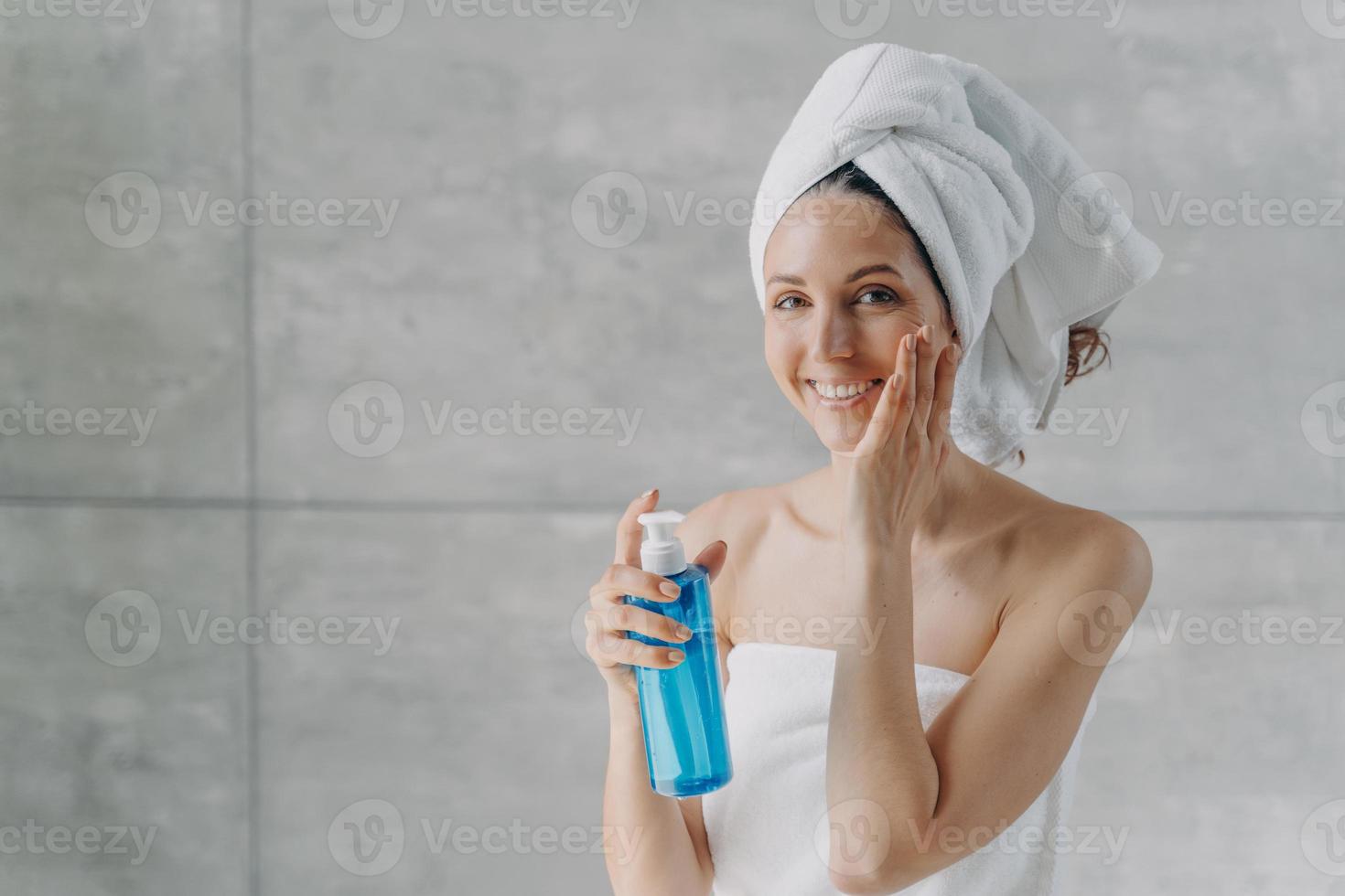 Face toner or micellar water. Gorgeous caucasian woman applying toner in flacon touching pure skin. photo