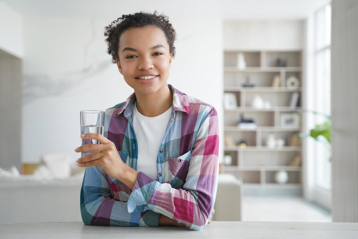 Happy african american girl drinks water from a glass. Healthy lifestyle, morning health routine. photo