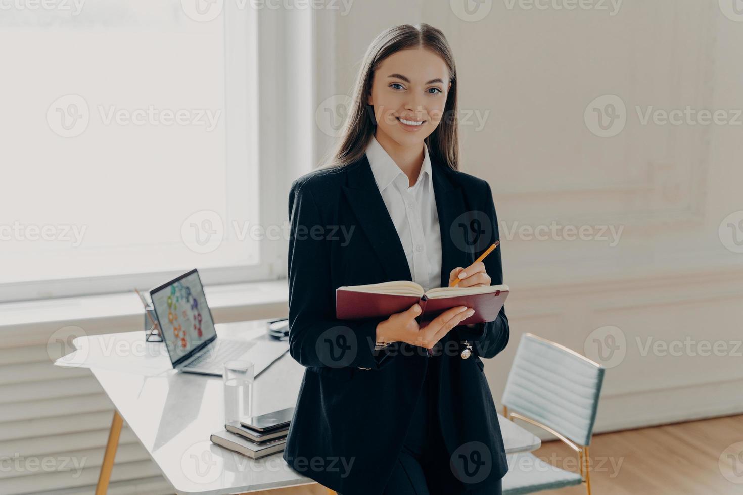 Female director holding notebook and pencil while leaning on office desk photo