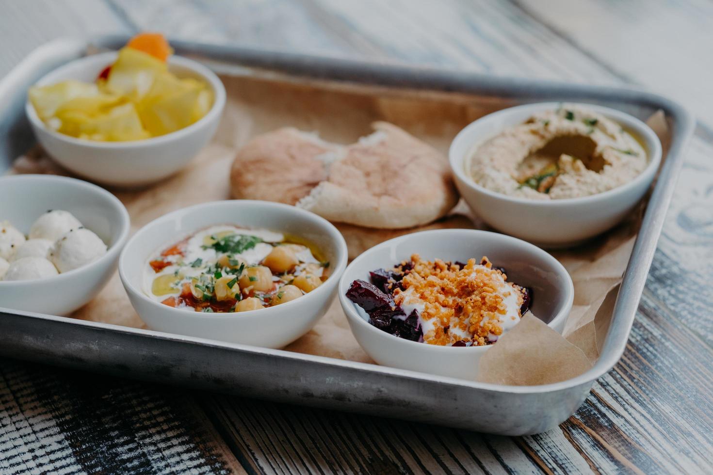 Food and nutrition concept. Traditional Israel dish for dinner. Tray of delicious hummus, beet with spices, core of tomatoes, pita bread, goat cheese served for you photo