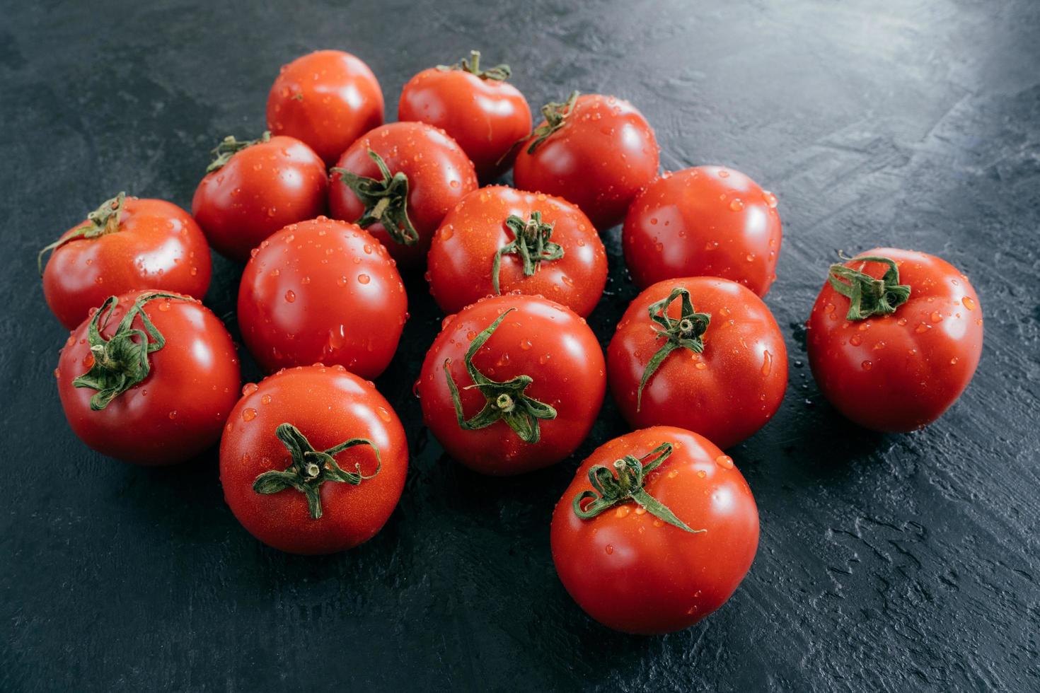 Ripe fresh red organic tomatoes being wet and clean, isolated over black background. Detailed close up shot. Selective focus photo