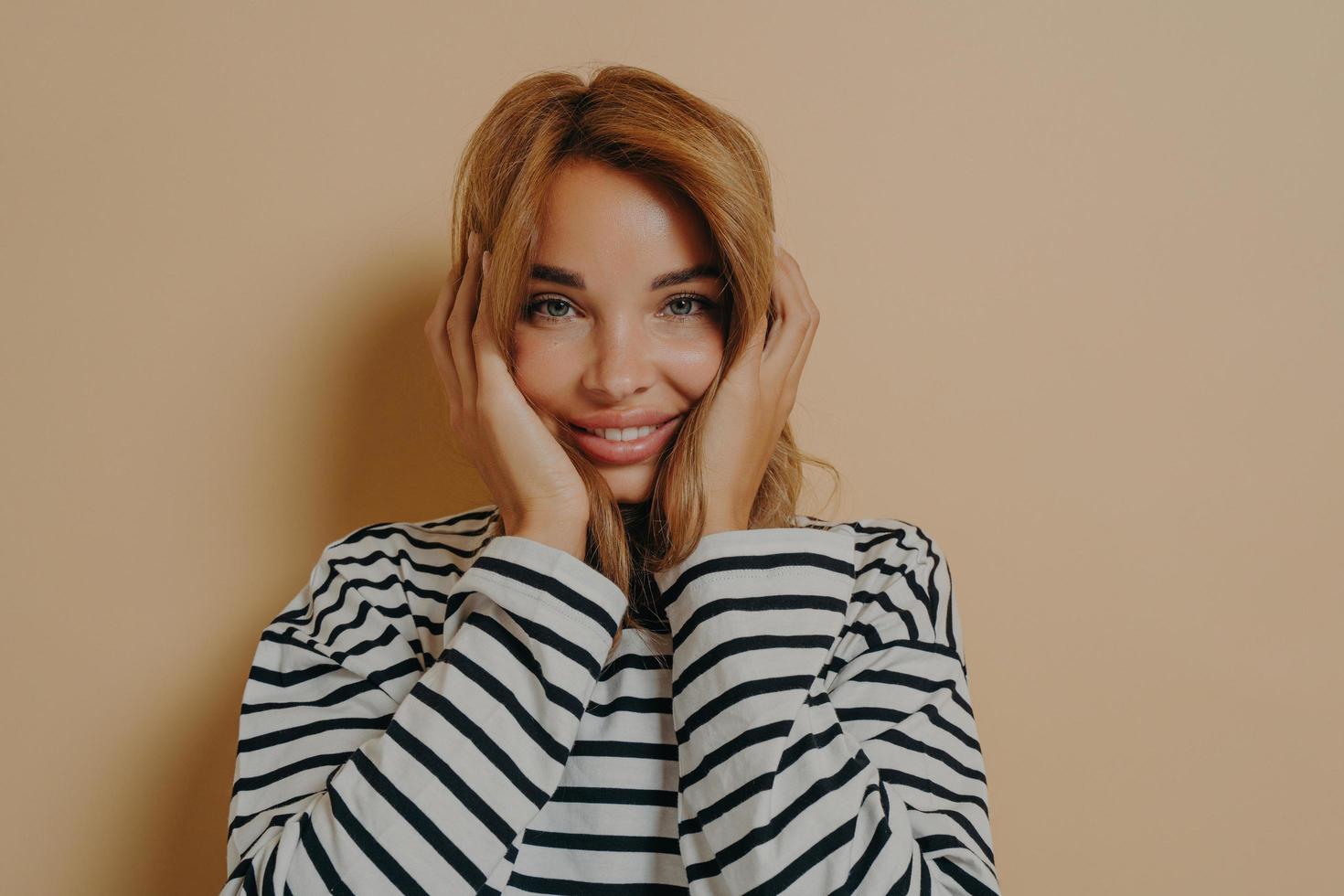 mujer joven feliz mirando a la cámara con expresión facial alegre sosteniendo su cara con ambas manos foto