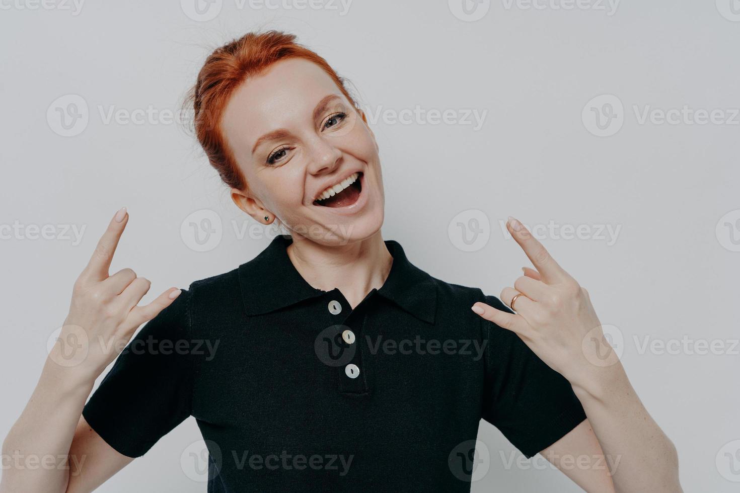Cheerful carefree ginger female in casual clothes showing heavy metal rock sign photo