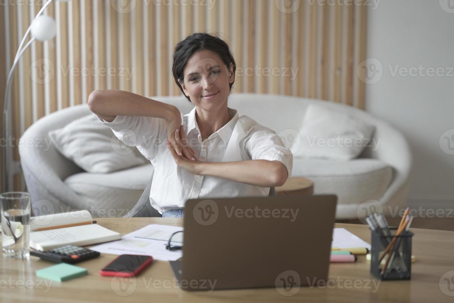 Positive business woman doing hands stretching exercises while listening to training lectures online photo