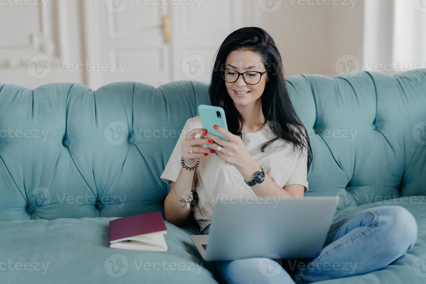 Happy female blogger chats with friends in social netwoks, works on laptop computer, poses in coworking space, sits on sofa in lotus pose, connected to wireless internet. Technology, freelancing photo