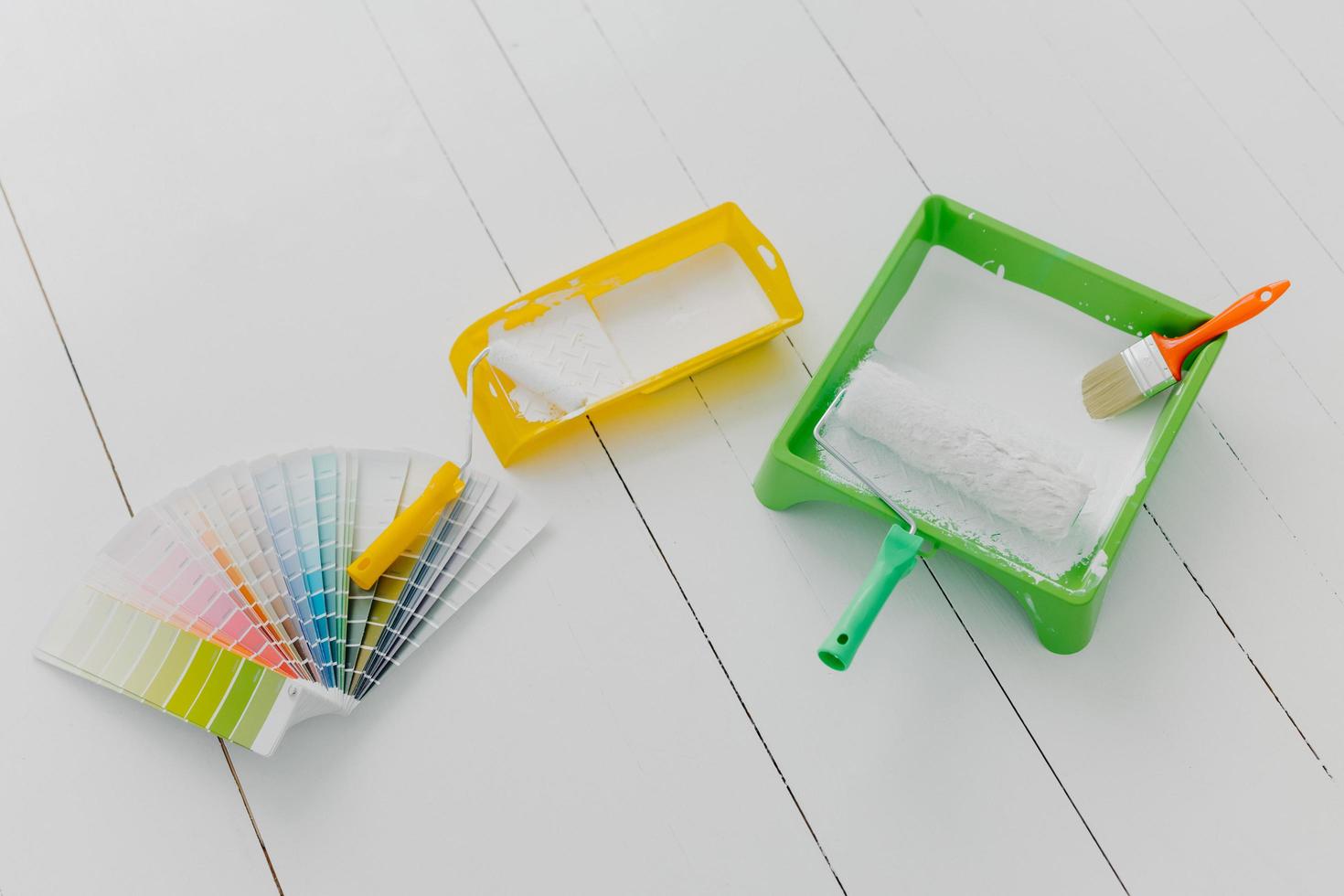 Top view of paint trays, brushes and rollers, color palette sample, white floor. Tools for making repairing and remodeling of house. Design concept photo