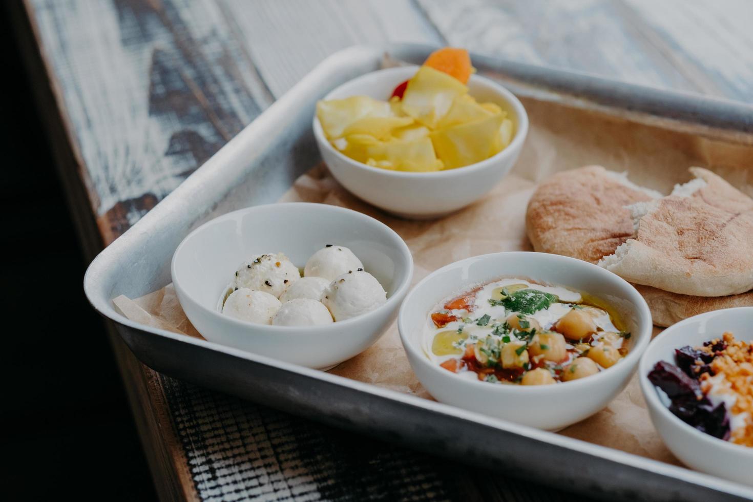 Tasty traditional dish concept. Cropped shot of tray with goat cheese, pita bread, grilled beetroot in bowls on wooden table. Israel food photo