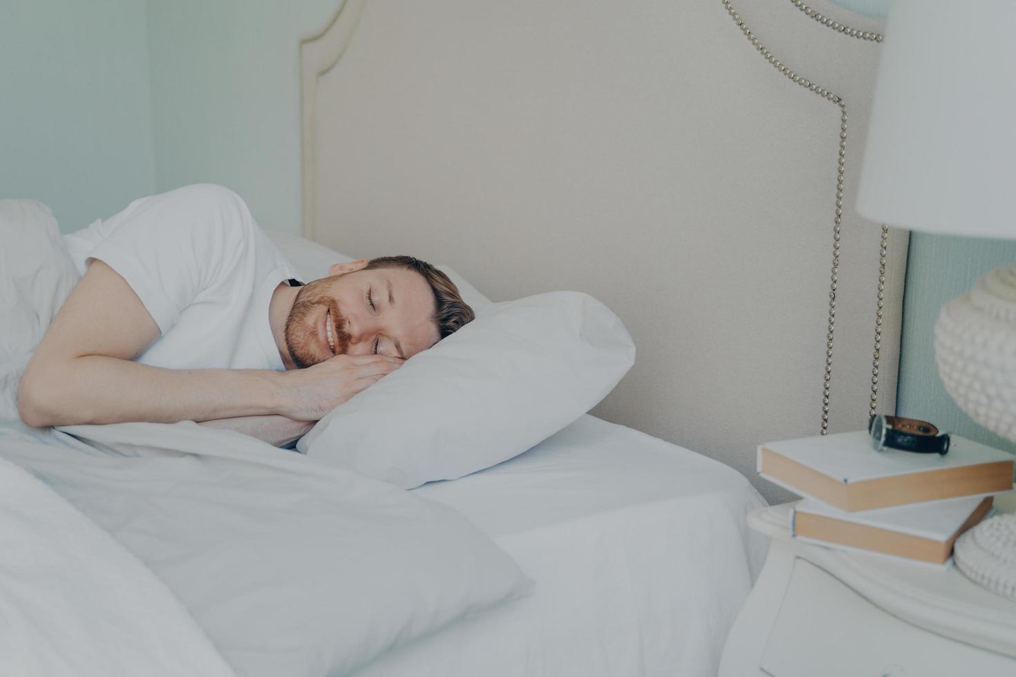 Young relaxed bearded man lying in bed with closed eyes photo