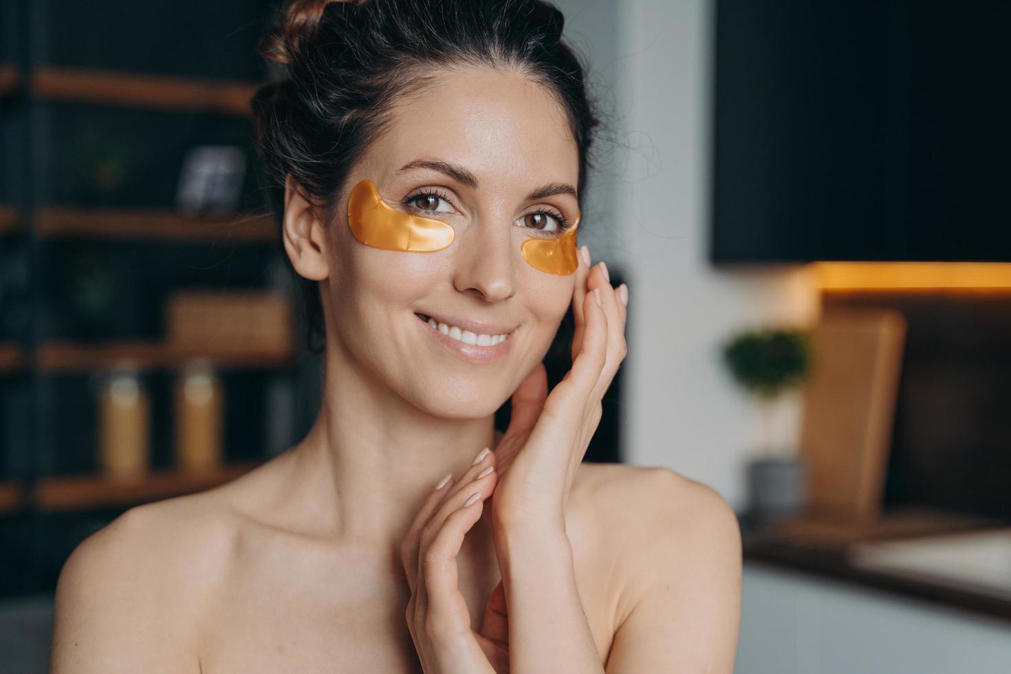 una joven sonriente aplica parches oculares de colágeno. Cosméticos, cuidado de la piel y rutina de belleza antiedad. foto