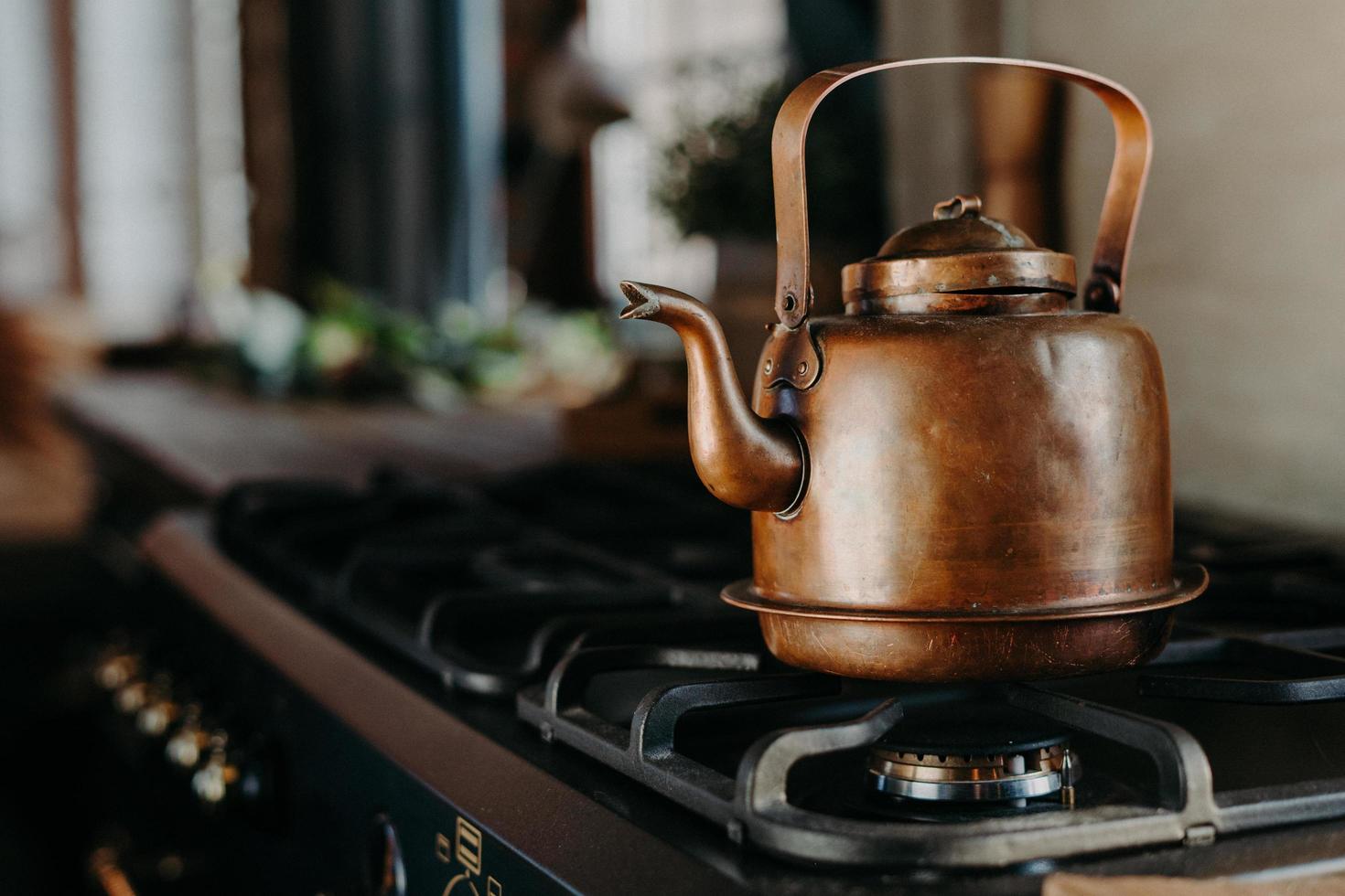 tetera de bronce en la cocina moderna. antigua tetera vintage en estufa de gas. preparando té. tetera de aluminio. luz del día soleada desde la ventana. foto