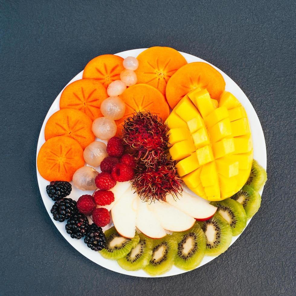 Slices of ripe exotic fruits on white plate. Kiwi, mango, raspberry, blueberry and persimmon. Fruits assortment. Top view. Healthy diet concept photo