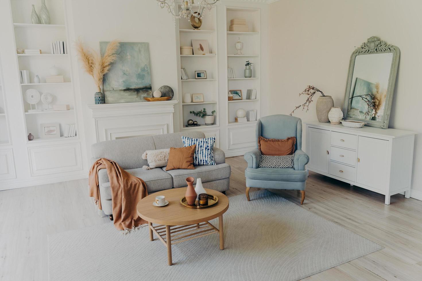 Modern home or cozy hotel room. Sofa and armchair, Mirror over chest, decoration and textile. photo