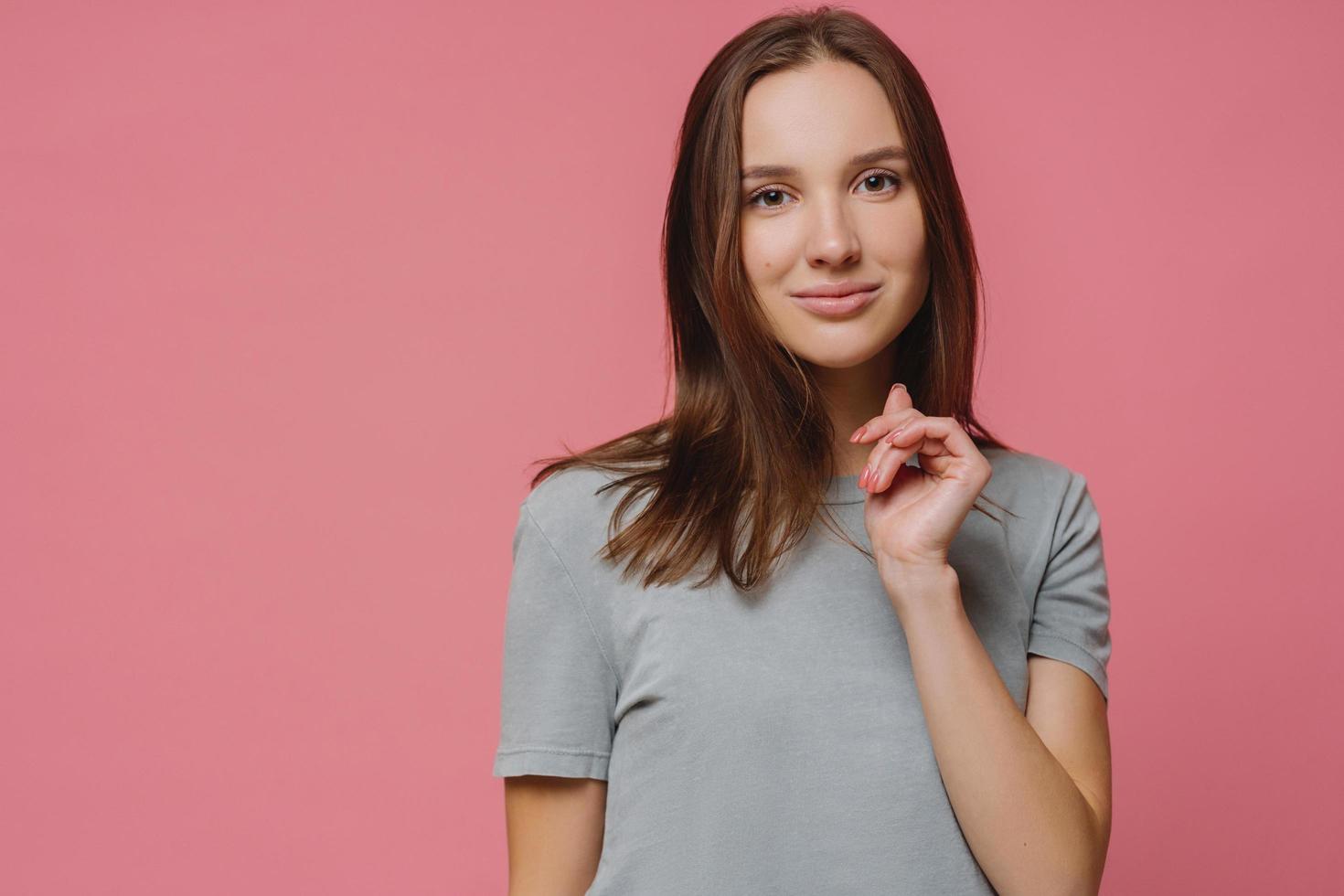 Confident lovely European woman has healthy pure skin, manicure, dressed in t shirt, enjoys photoshoot, models against rosy background with copy space, hears something pleasant or interesting photo