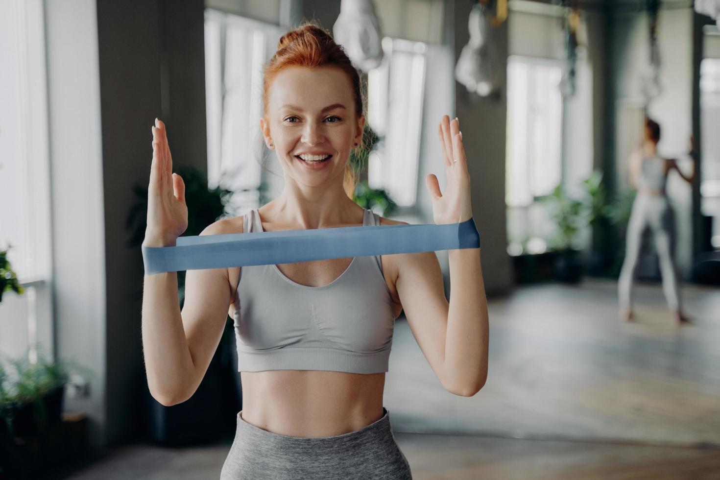 Portrait of young sporty redhead woman in sportswear with resistance rubber band photo