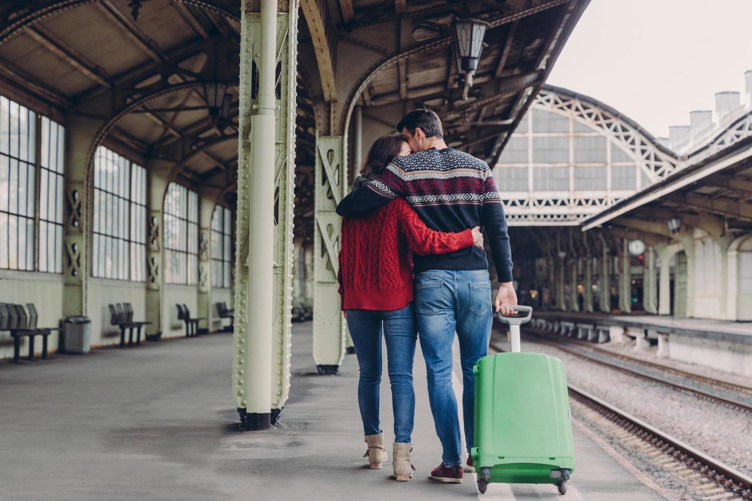 Relationship and travelling concept. Lovely woman and man cuddle while walk across railway station platform, carry suitcase, express love and support, stand closely to each other, have journey photo