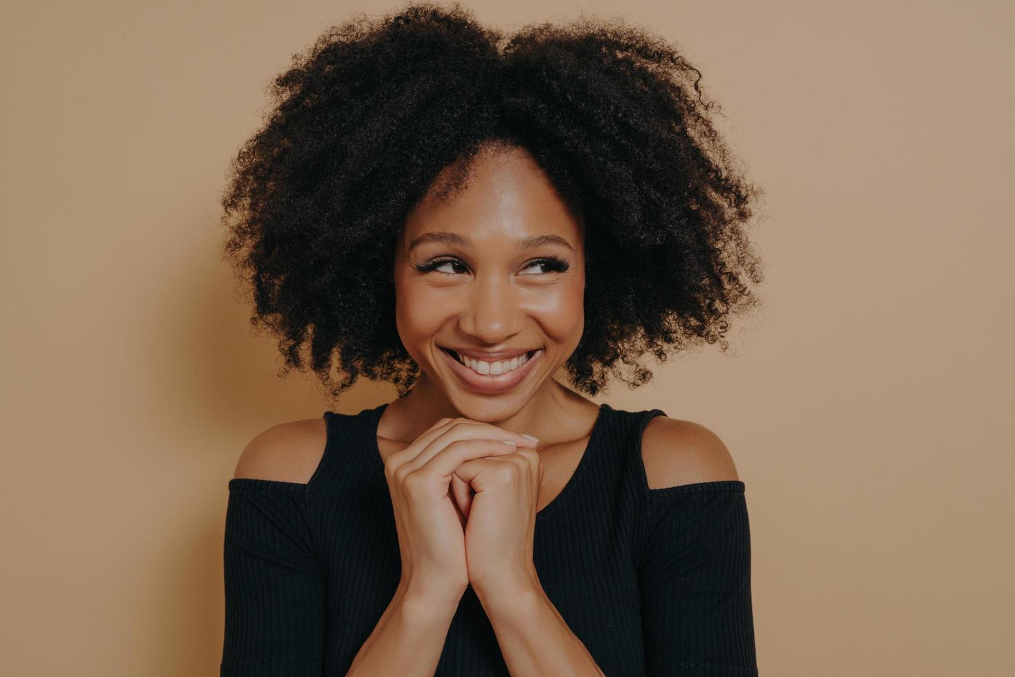 Studio shot of happy Afro girl keeps hands together under chin photo