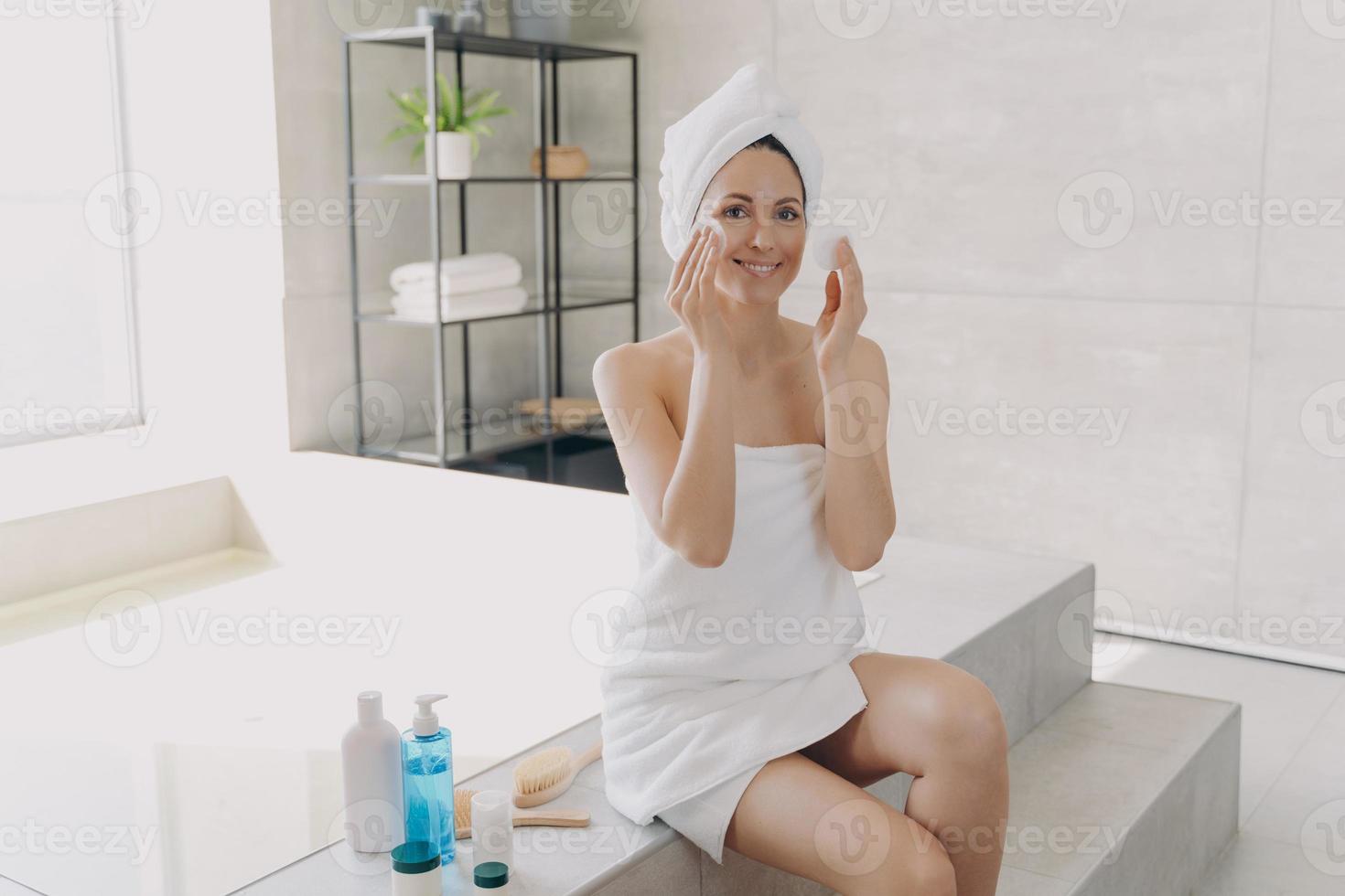 Happy girl applying face lotion with cotton disks. Skin purifying and spa procedures at home. photo