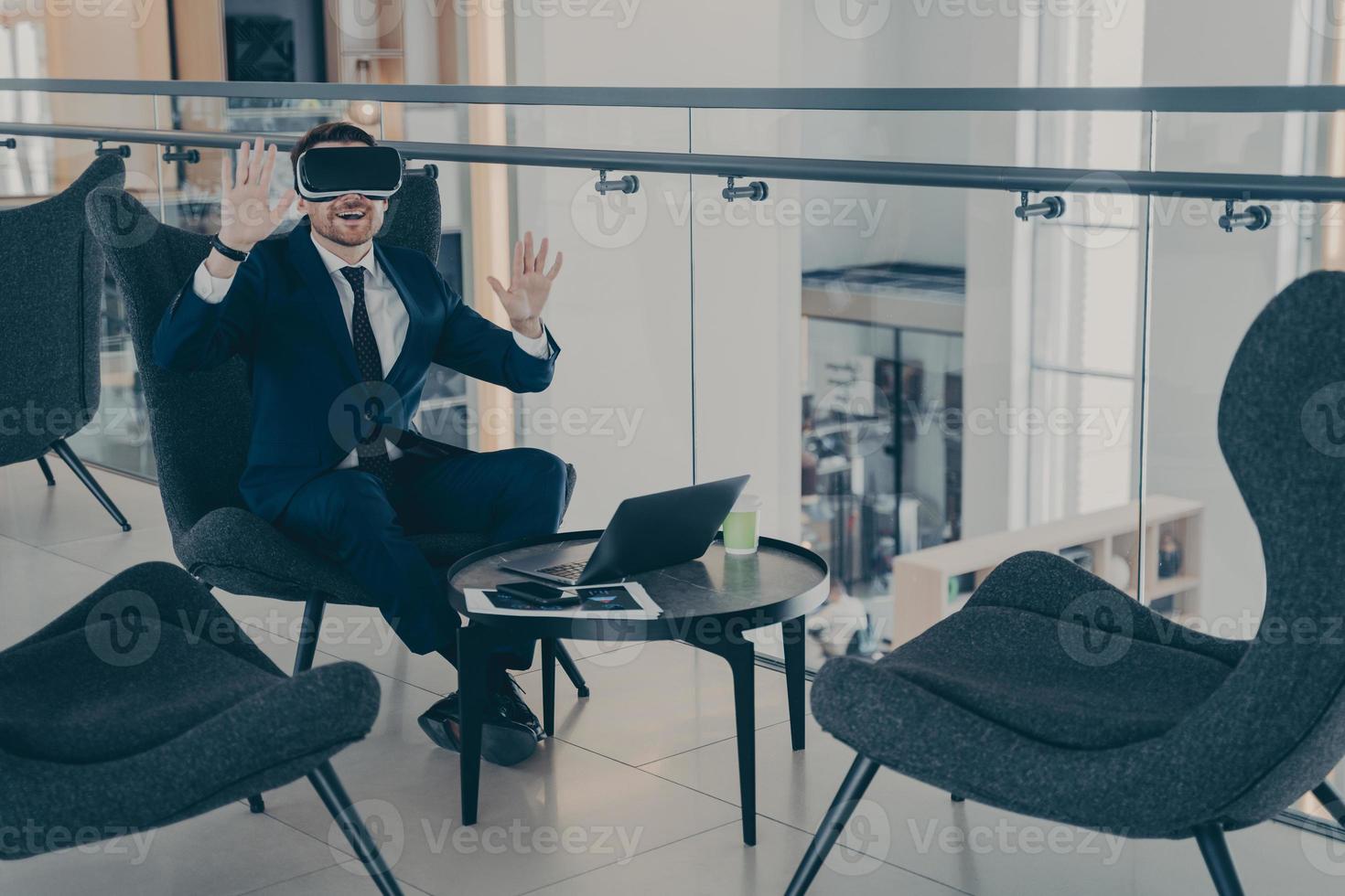 Businessman sitting in reception area of office centre during his coffee break in VR headset photo