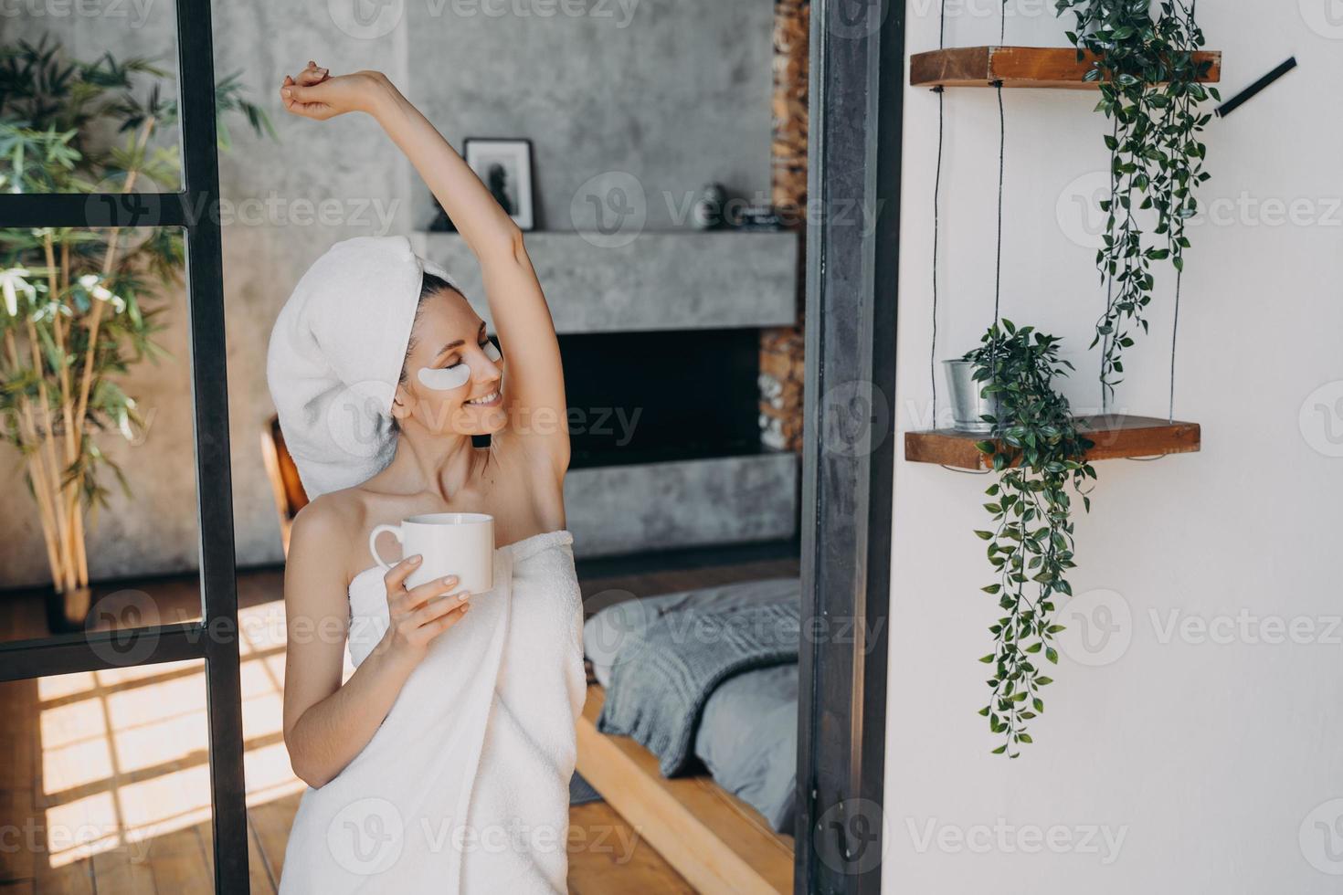 una mujer joven con una taza de té aplica parches antiarrugas para los ojos y se relaja. vacaciones en balneario. foto